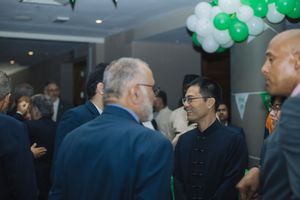 People having a conversation at an indoor event with green and white balloon decorations.