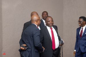 A group of men in business suits engaged in conversation while standing in a hallway.