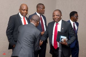 A group of businessmen in dark suits and red ties gather in conversation at a professional meeting.
