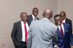 Business professionals in suits having an animated conversation in front of a light colored wall.