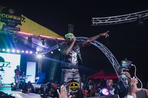 Hip hop performer on stage with arms spread during energetic concert performance with dramatic lighting and stage rigging.