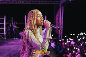 A performer sings on stage with pink and purple lighting during a live concert performance.