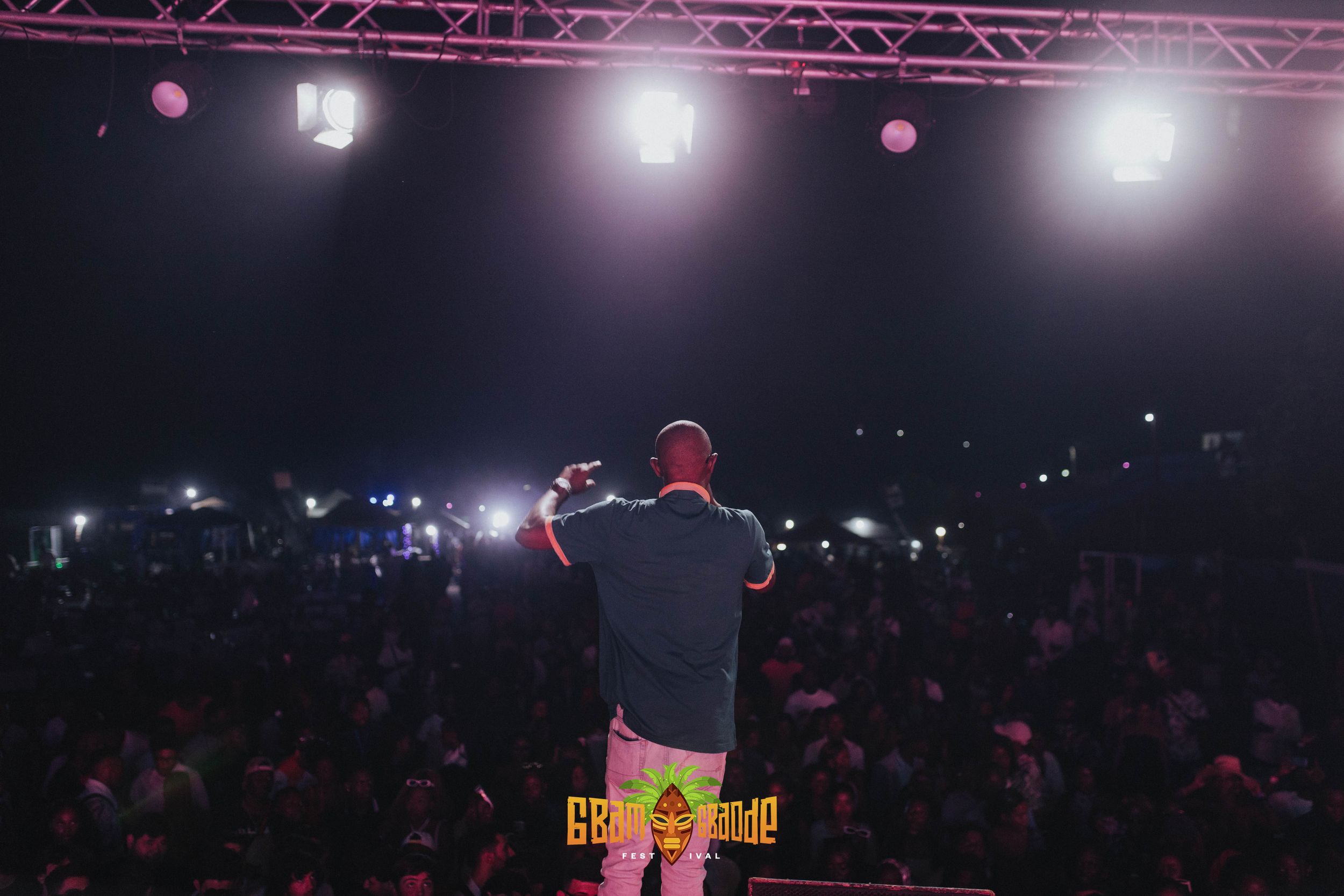 Concert performer stands on stage silhouetted against bright lights while crowd holds up phone lights in dark venue.