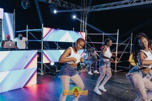 Performers dancing energetically on stage with colorful geometric backdrop panels and dynamic lighting setup.