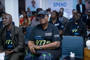 Attendees in branded t-shirts smile while seated at a business event or conference.