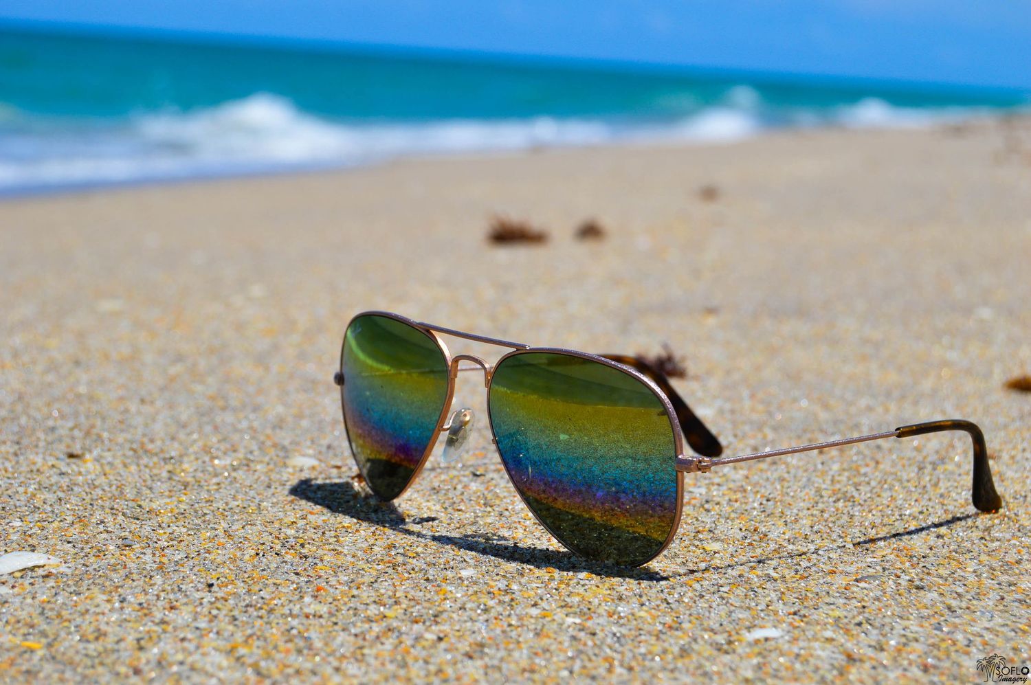Reflective sunglasses lying on sandy beach with ocean waves in the background.