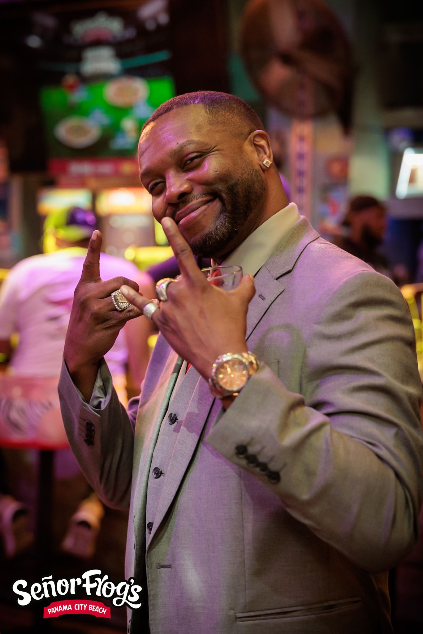 A joyful performer in a gray suit gestures with both hands at a nightclub event.