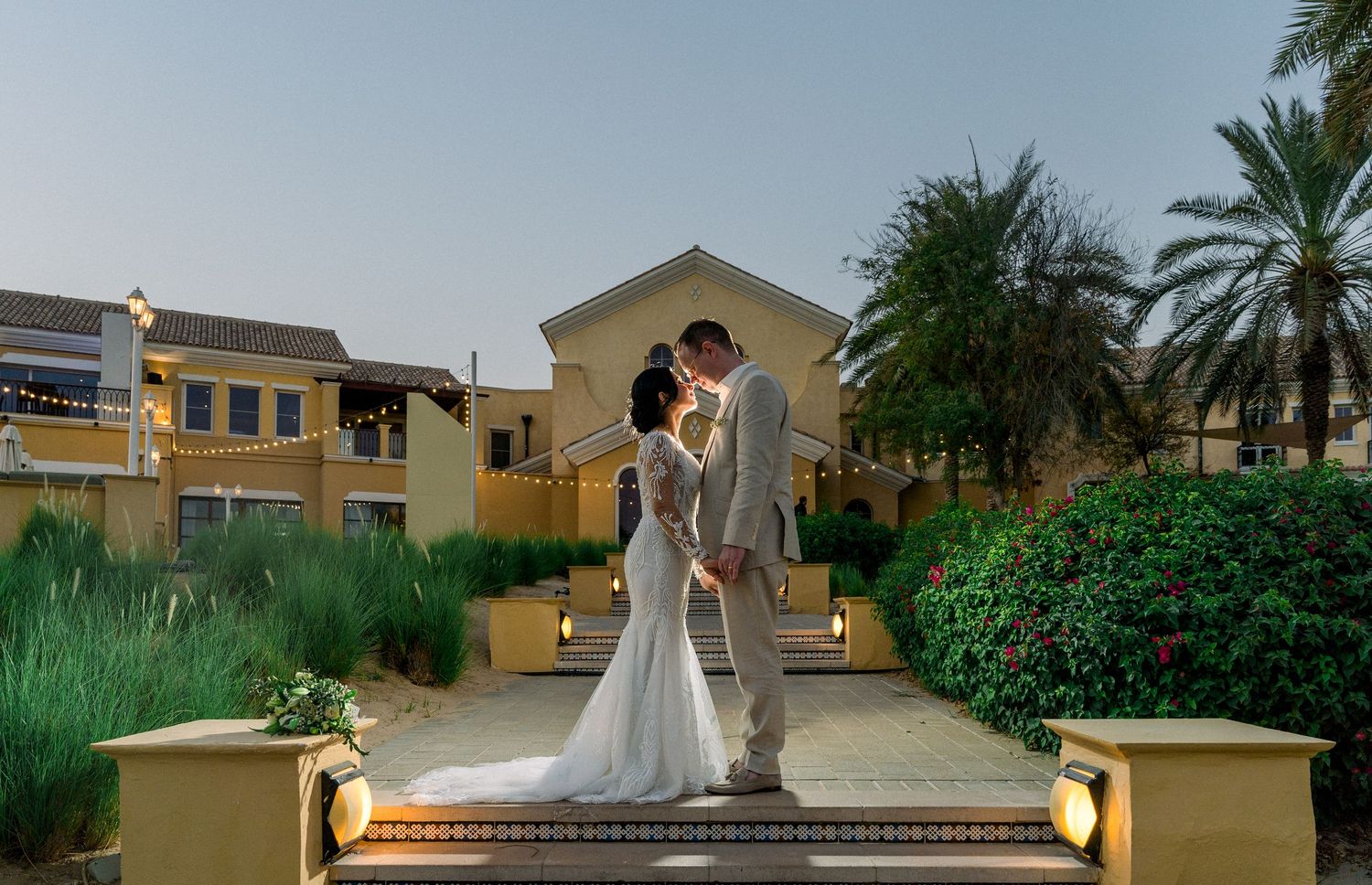 Aerial view of an elegant outdoor wedding reception with tables arranged around a green lawn dance floor surrounded by palm trees.