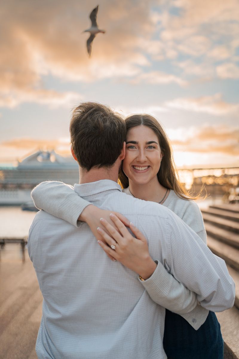 woman smiles into the camera while huggin her boyfriend who just proposed during a proposal photoshoot in Sydney