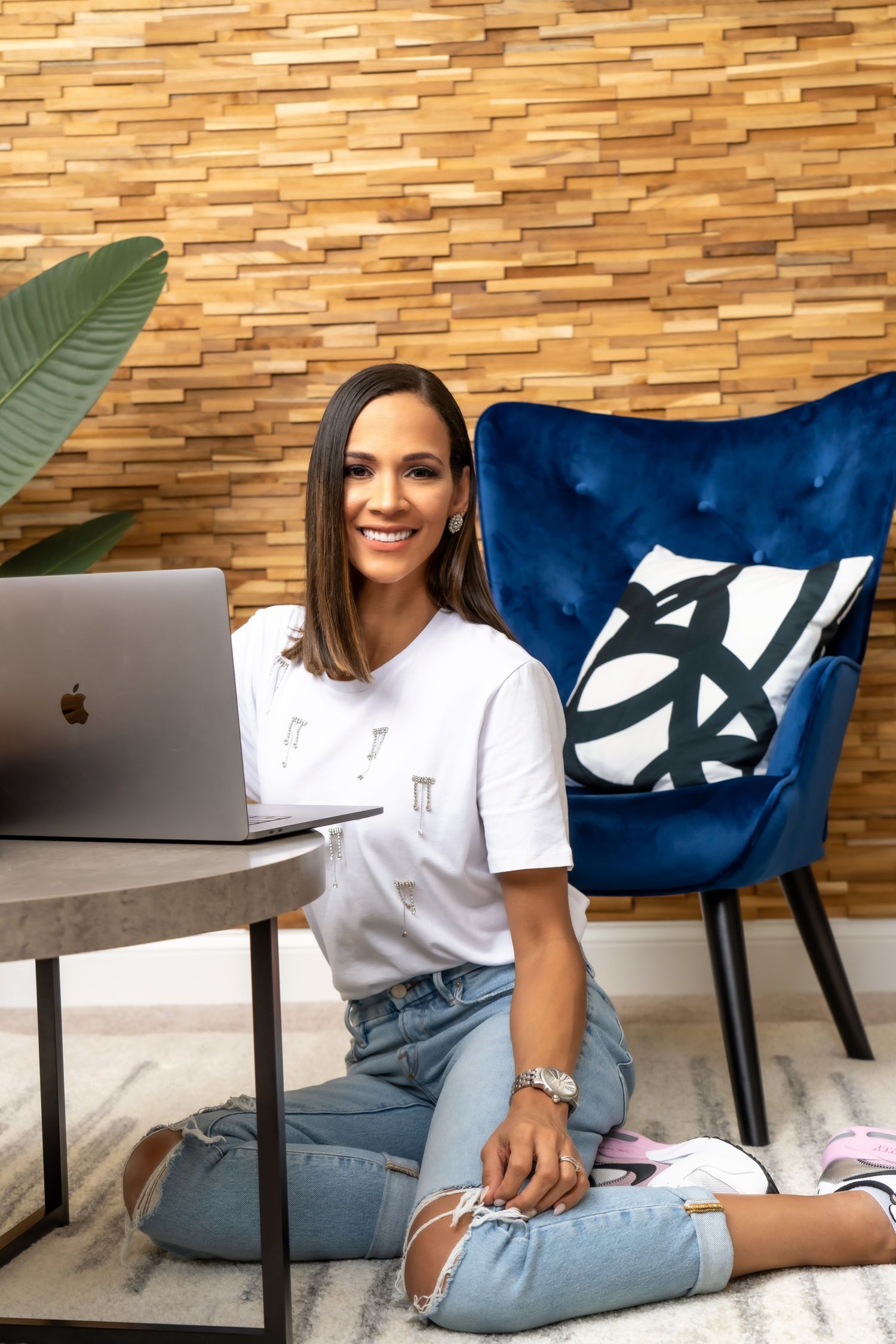 Professional sitting casually at desk with laptop and decorative wall background.