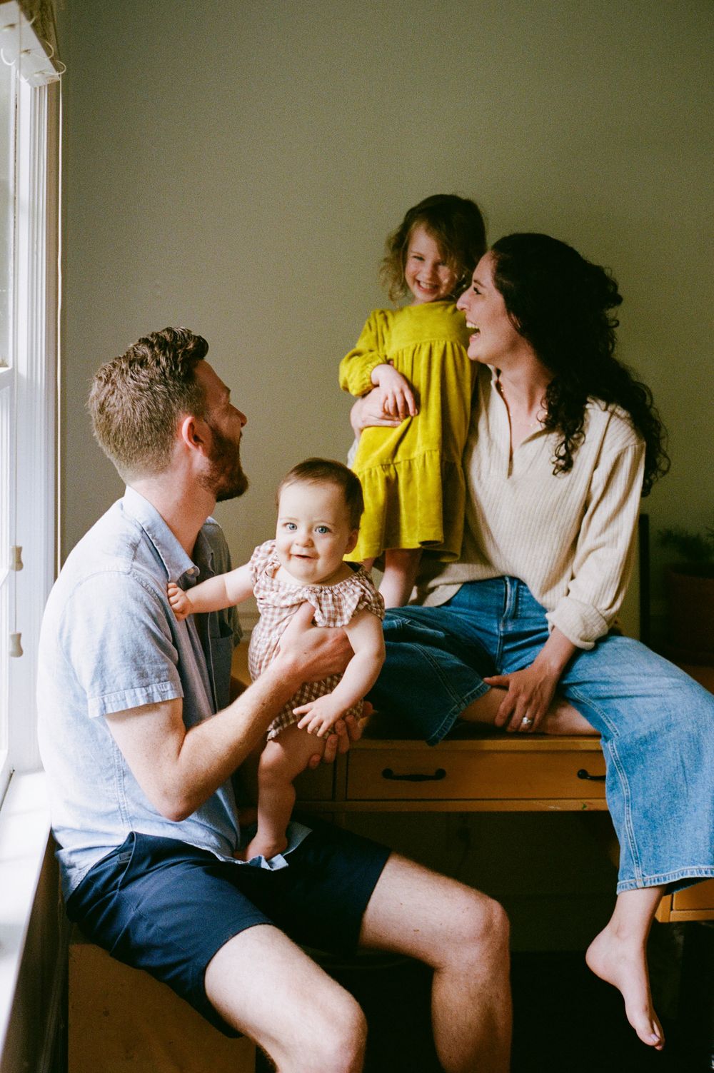 A joyful family moment by a window with children sitting on a wooden dresser.