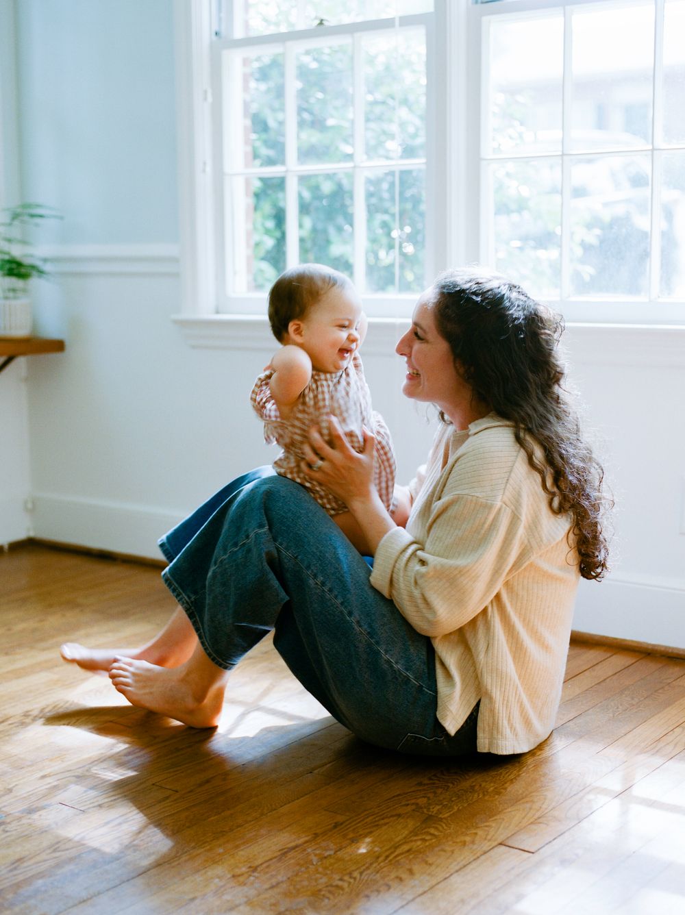 A joyful moment shared between parent and child sitting together on a sunlit hardwood floor near bright windows.