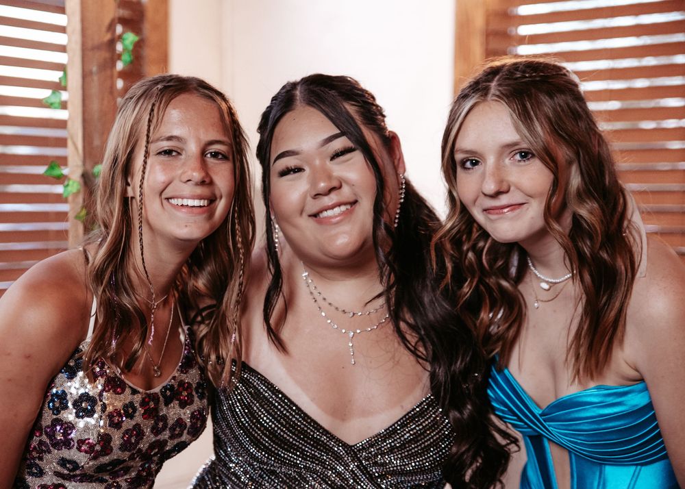 Three young people in formal attire pose together and smile at a social gathering.