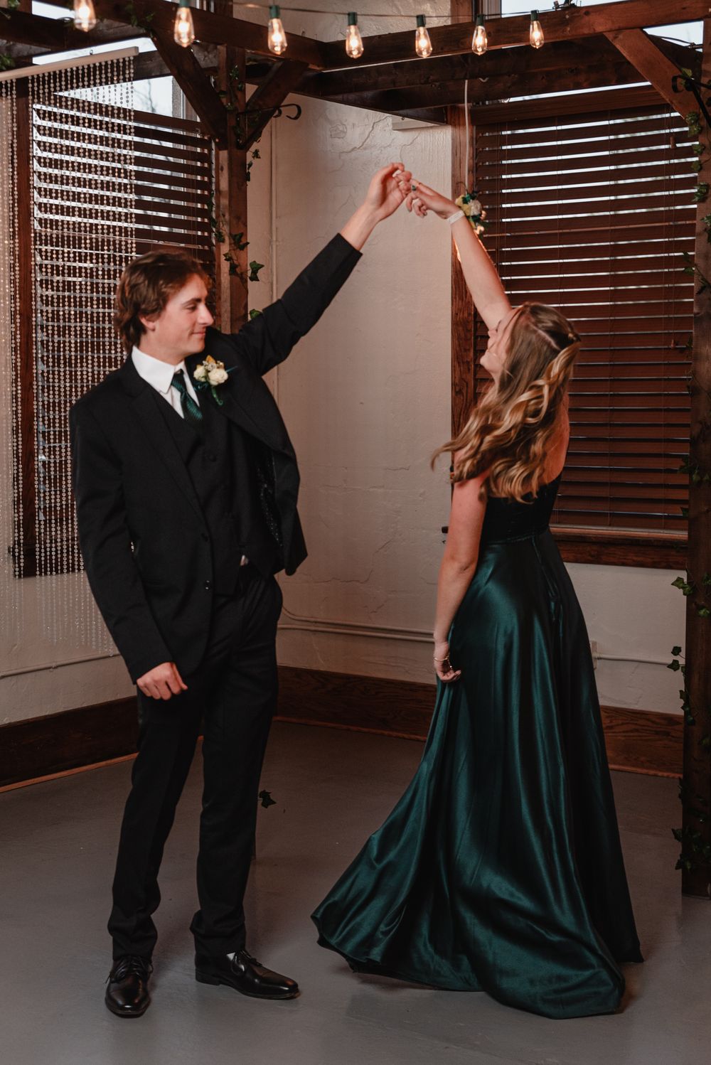 A couple dancing together at a formal event, with the woman wearing an emerald green gown and the man in a dark suit.