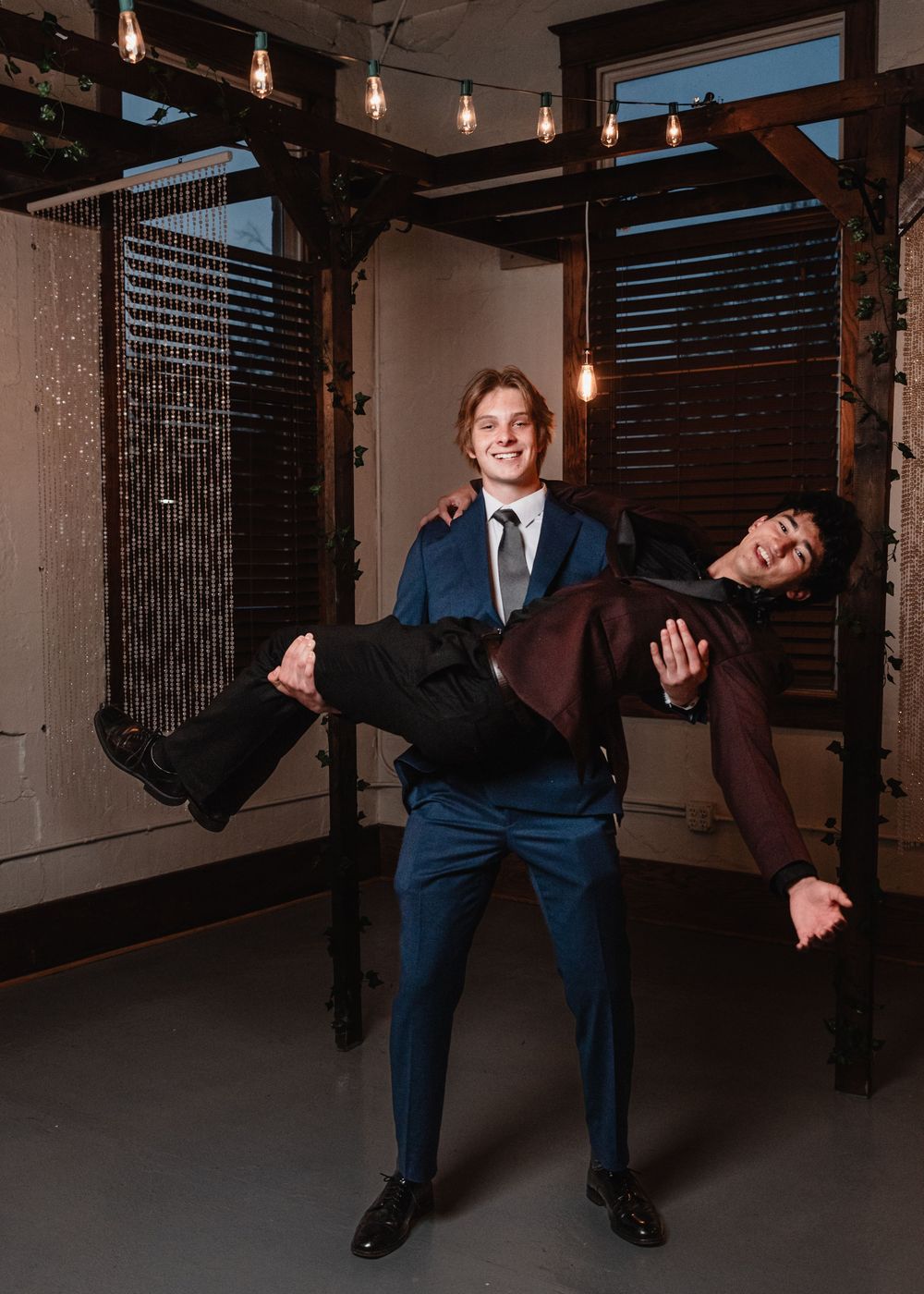 Playful wedding photo showing the groom holding the bride in a warm, modern industrial loft with exposed beams and hanging lights.