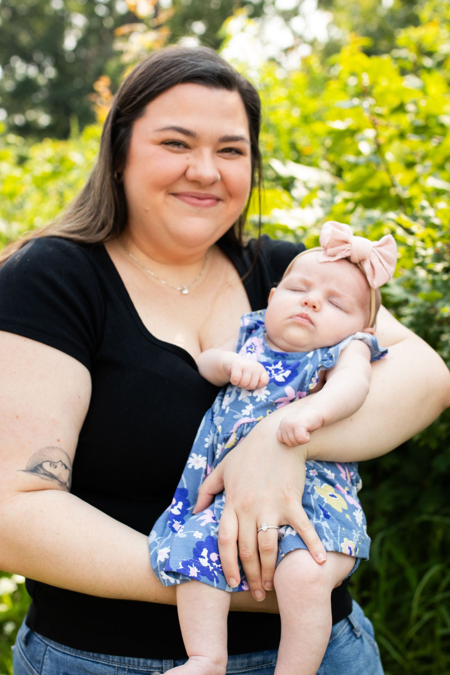 Parent holding and playing with baby wearing blue floral outfit in outdoor garden setting.