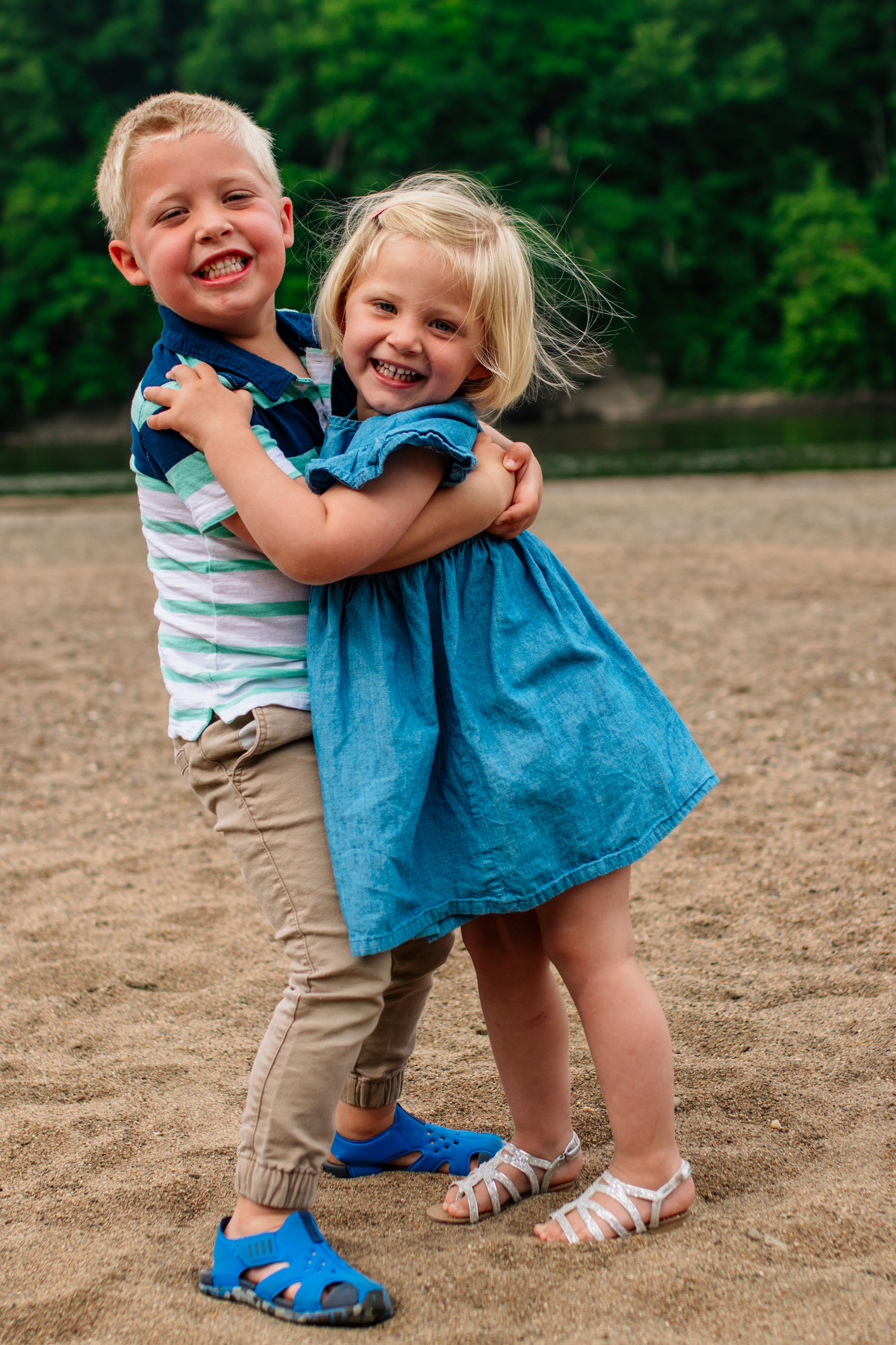 Two children hugging and laughing together on sandy ground.