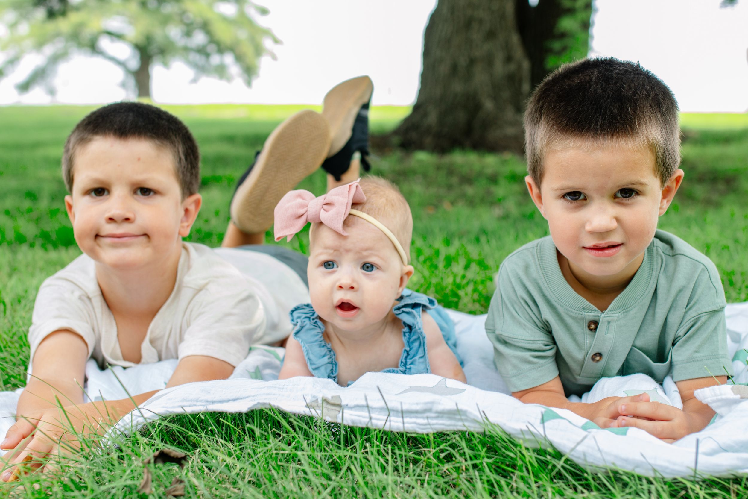 Three children lying on a blanket in the grass on a summer day.