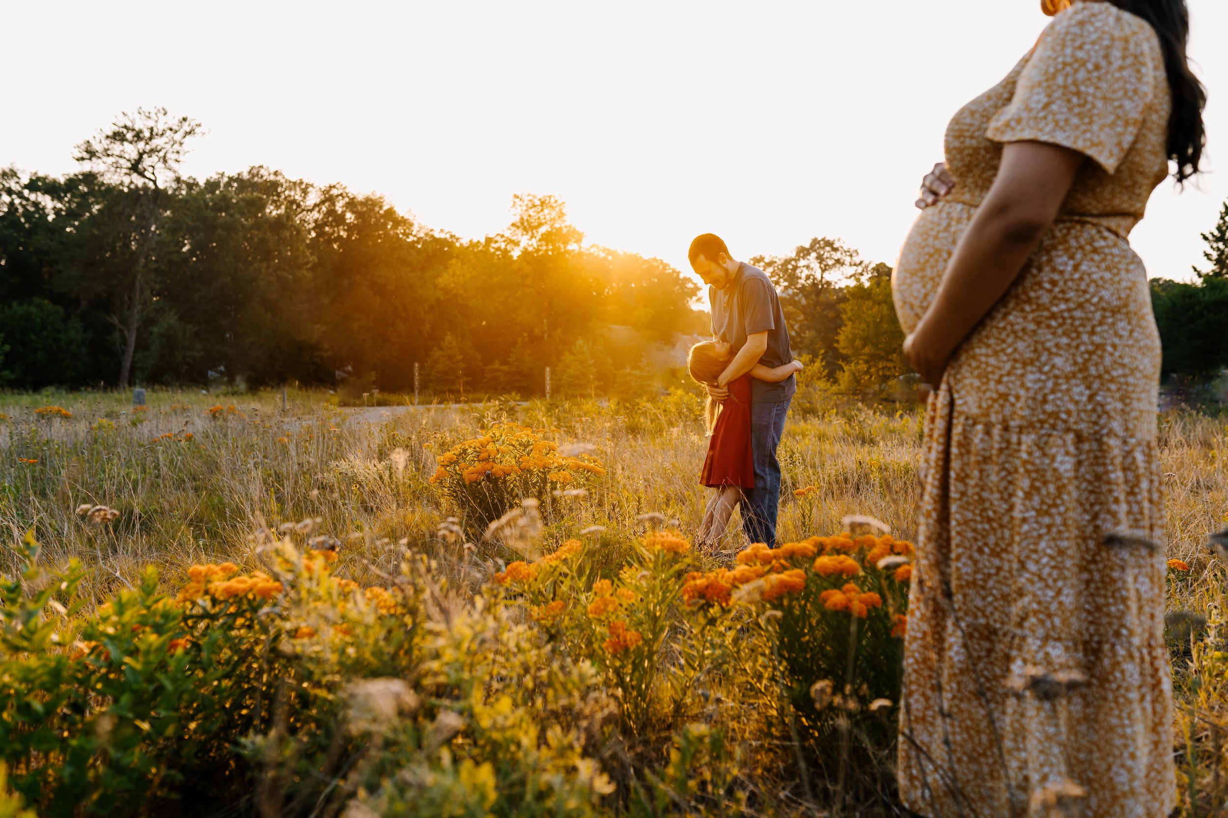 Mom stands holding her belly and lovingly while her husband and daughter hug during photos with knoxville photographer