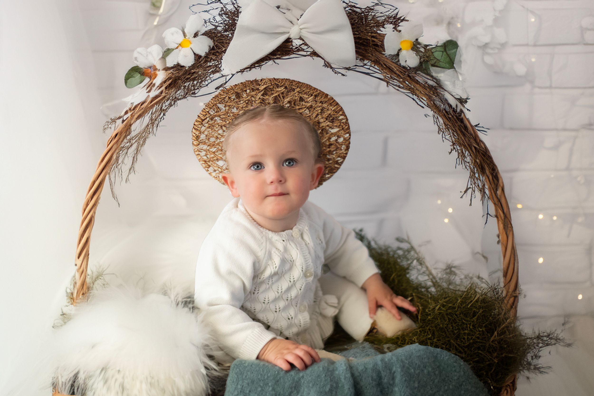 Whimsical spring portrait with woven floral arch, rustic straw hat, cozy white sweater, and natural woodland elements.