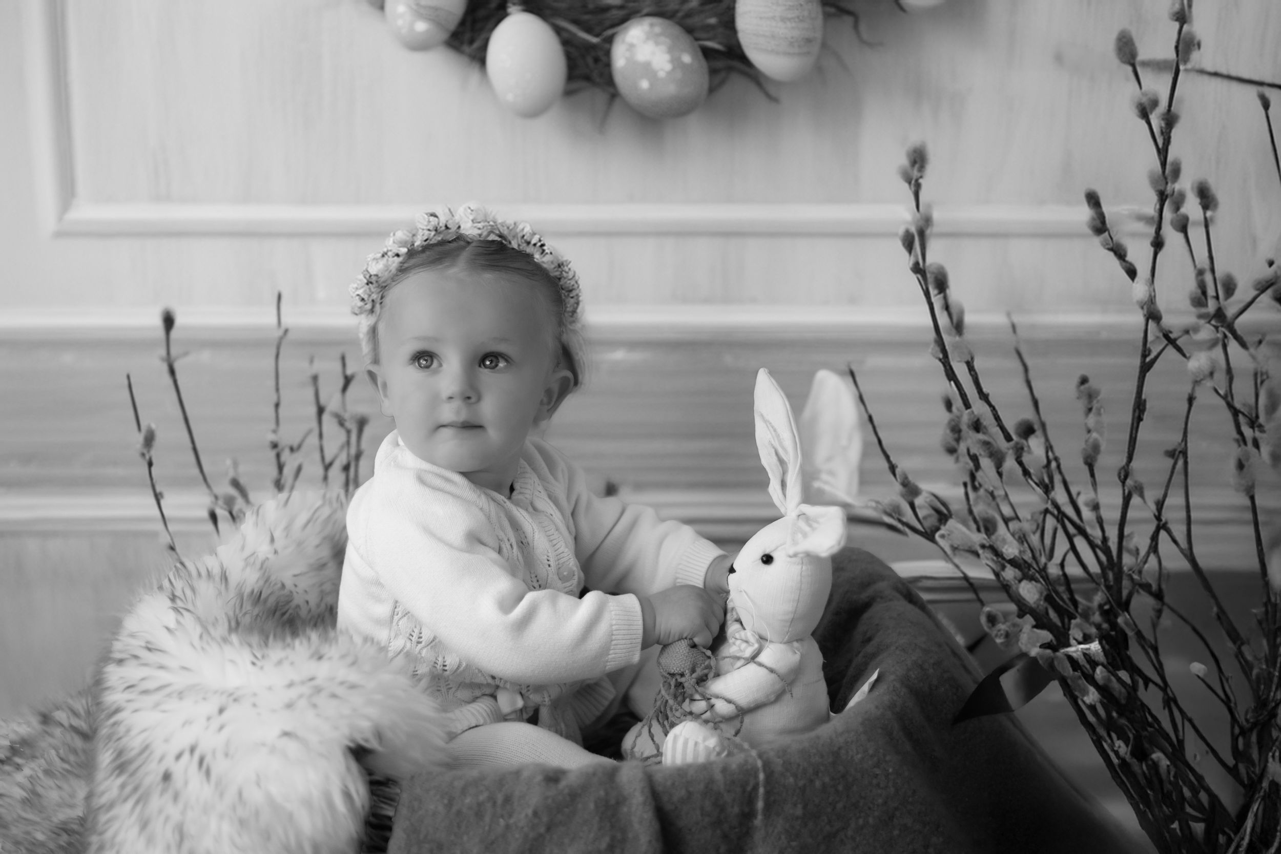 Black and white vintage-style portrait with a plush bunny toy and spring branches, set in a soft interior scene.