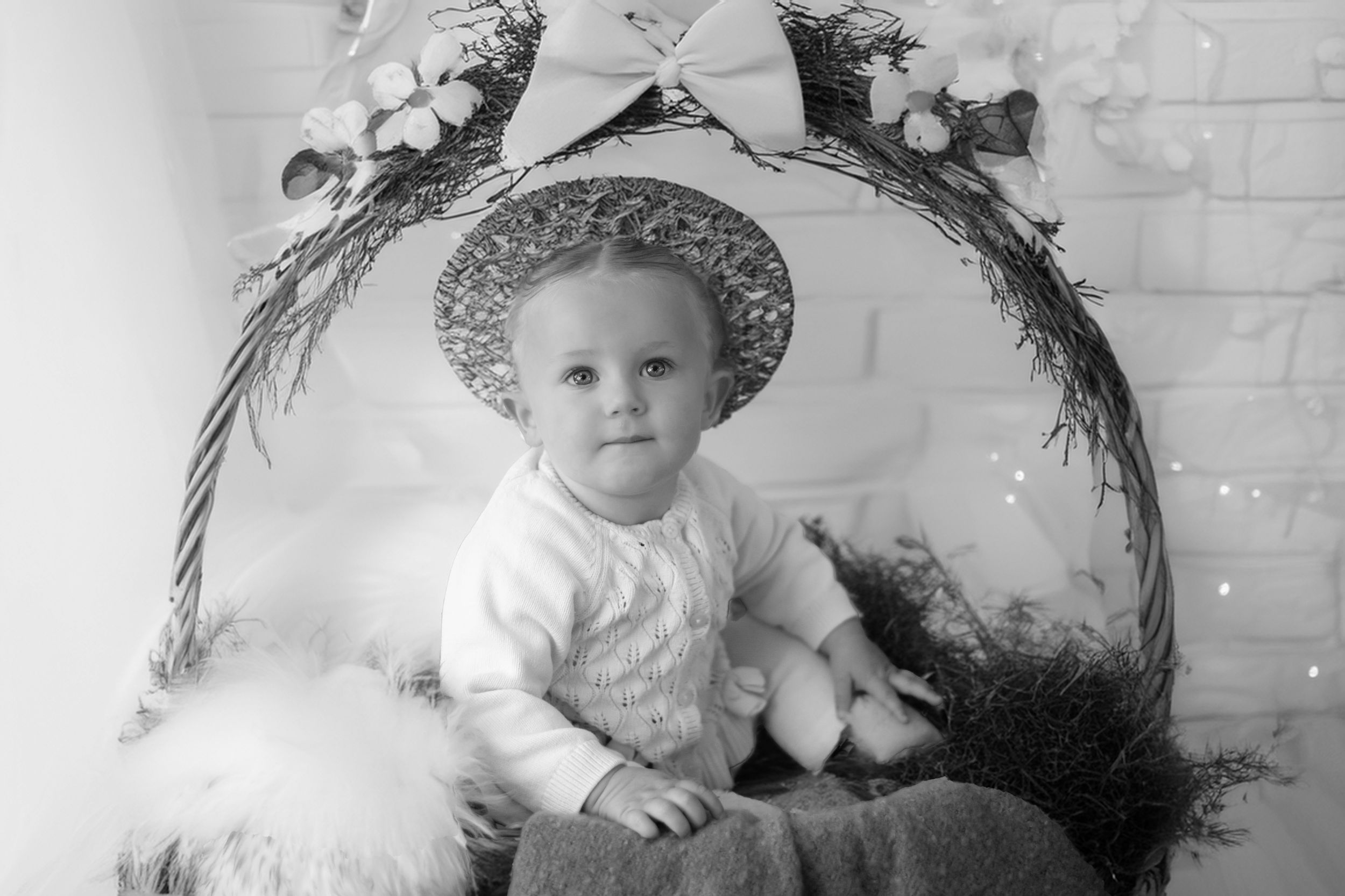 Vintage black and white portrait photograph showing a young child wearing a decorative hat and white outfit.