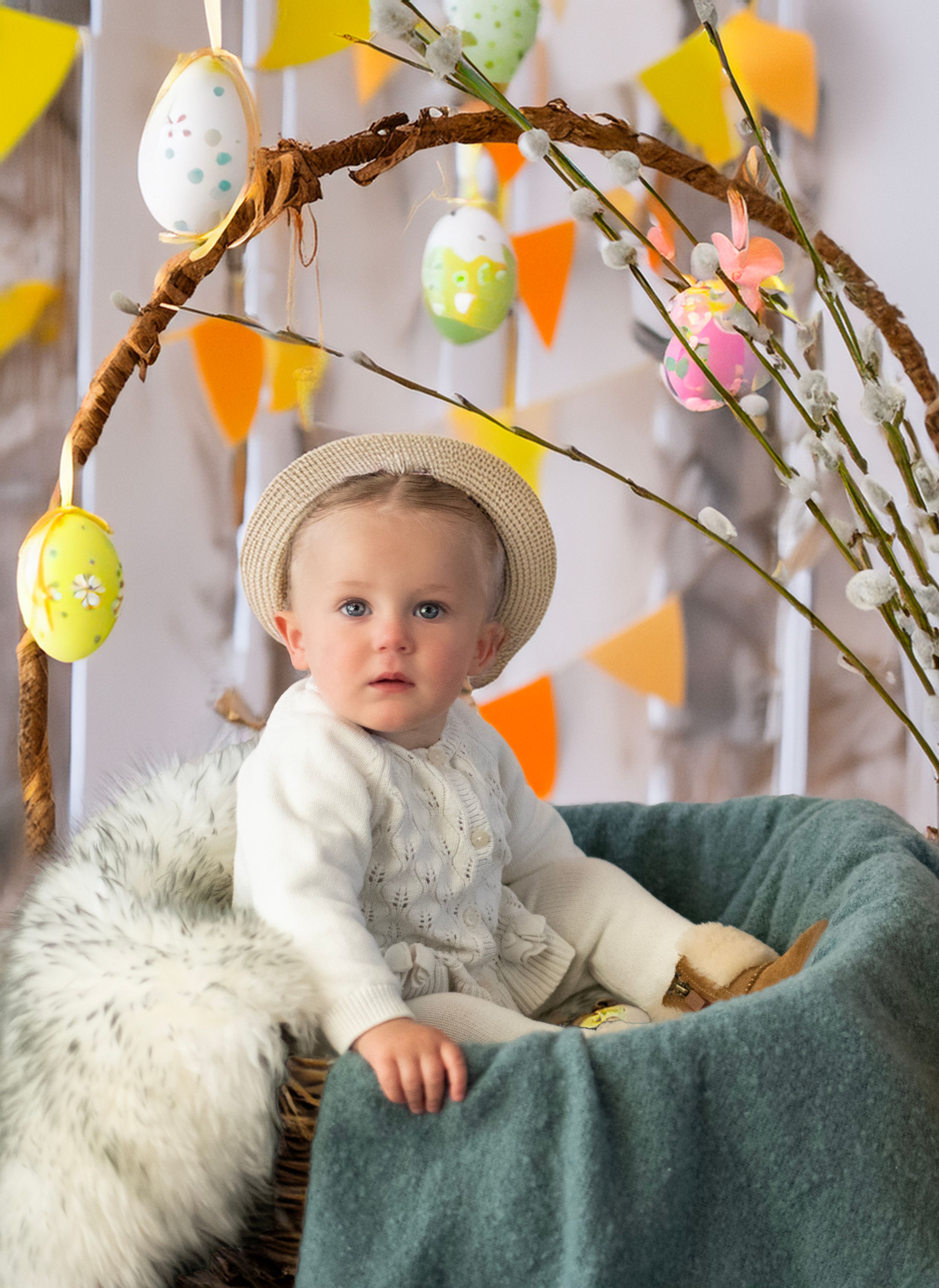 Easter decorations with colorful eggs on branches and triangular banners hang above a cozy chair with blanket and straw hat.