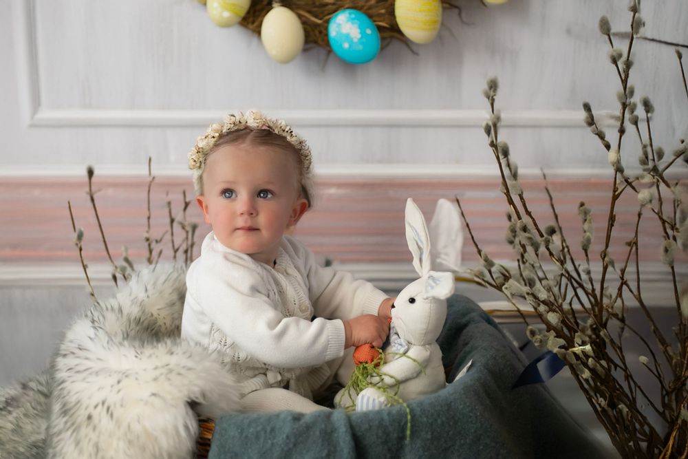Easter spring photo setup with white plush bunny, colorful eggs, and floral decorations against a pink wall.