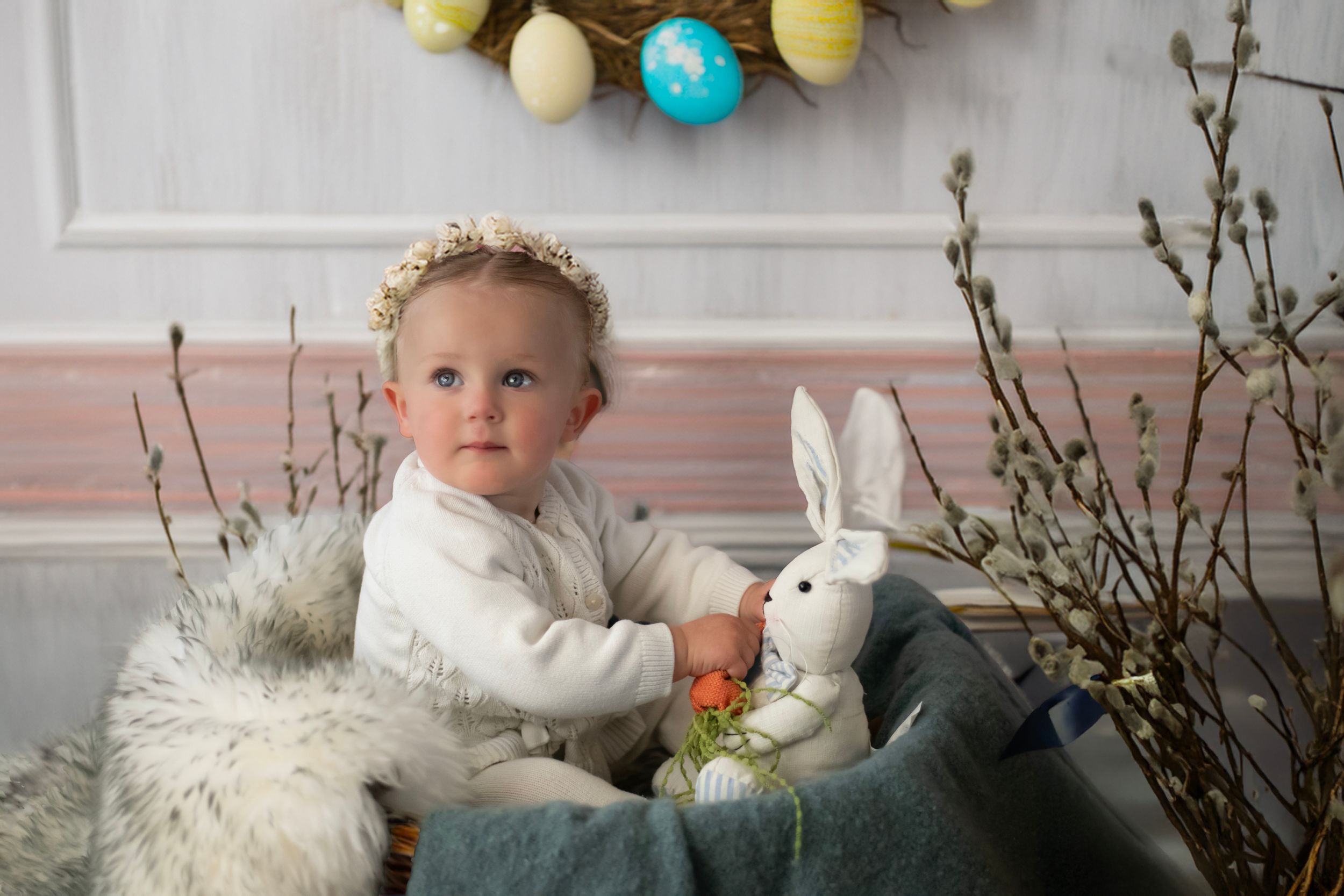 Easter spring photo setup with white plush bunny, colorful eggs, and floral decorations against a pink wall.