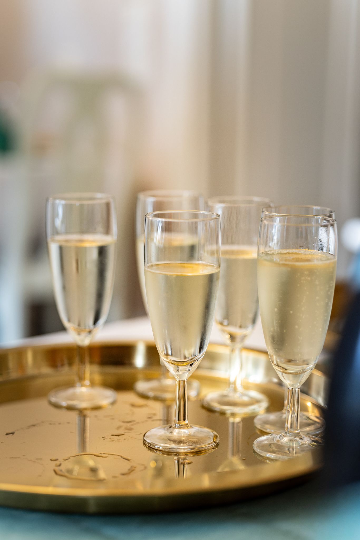 Several champagne flutes filled with sparkling wine arranged on a golden tray at an elegant celebration event.