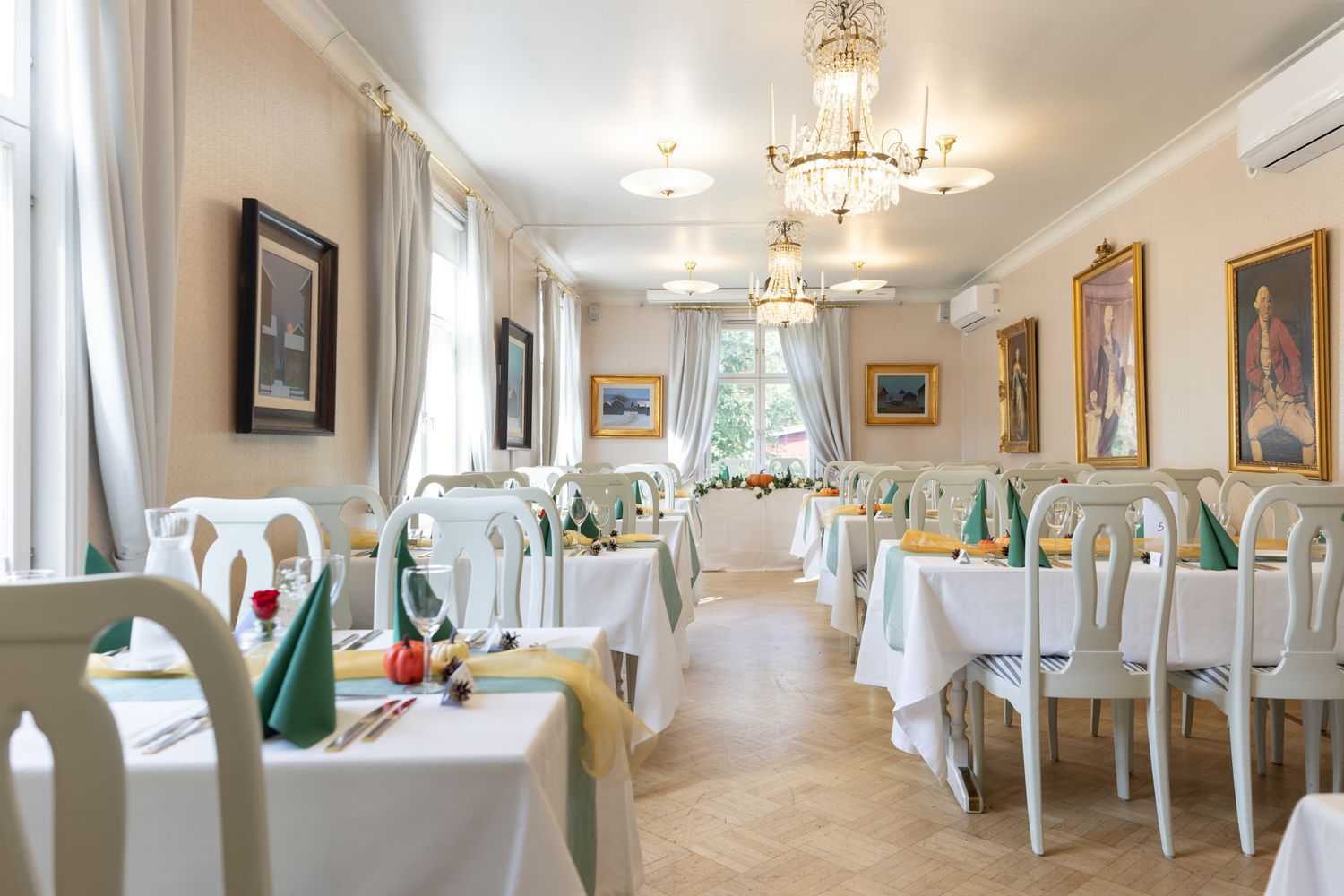 Elegant restaurant dining room with white tables, green accents, chandeliers, and classic portrait paintings on walls.