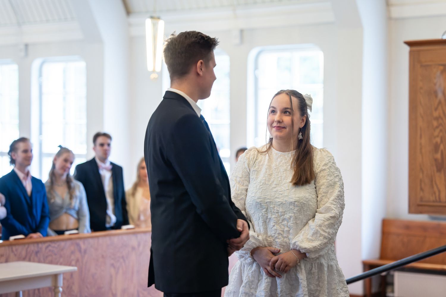 Bride and groom exchange vows at a church wedding ceremony, with guests seated in pews behind them.