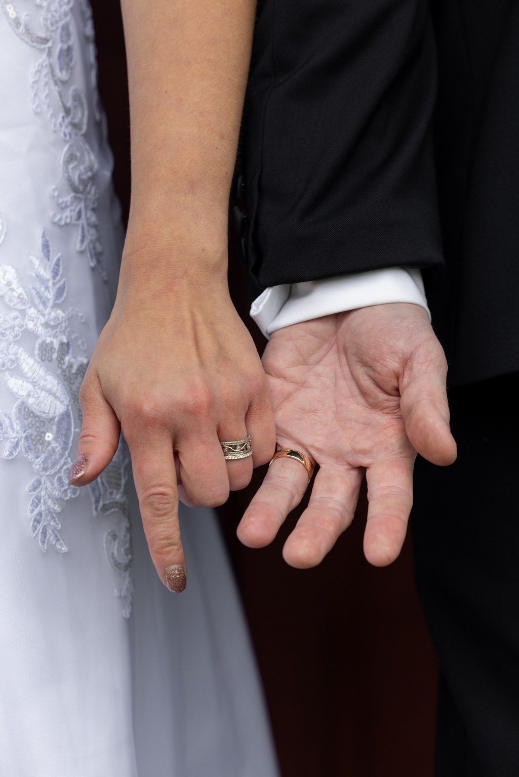 Close-up of bride and groom's hands showing their wedding rings against white dress and black suit.