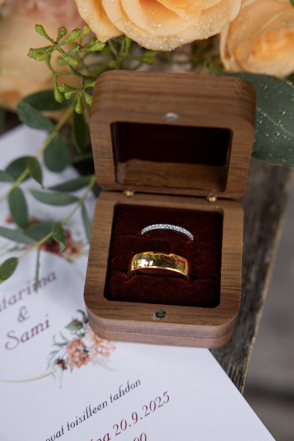 Wedding rings displayed in wooden boxes alongside wedding invitation details on a decorated table setting.
