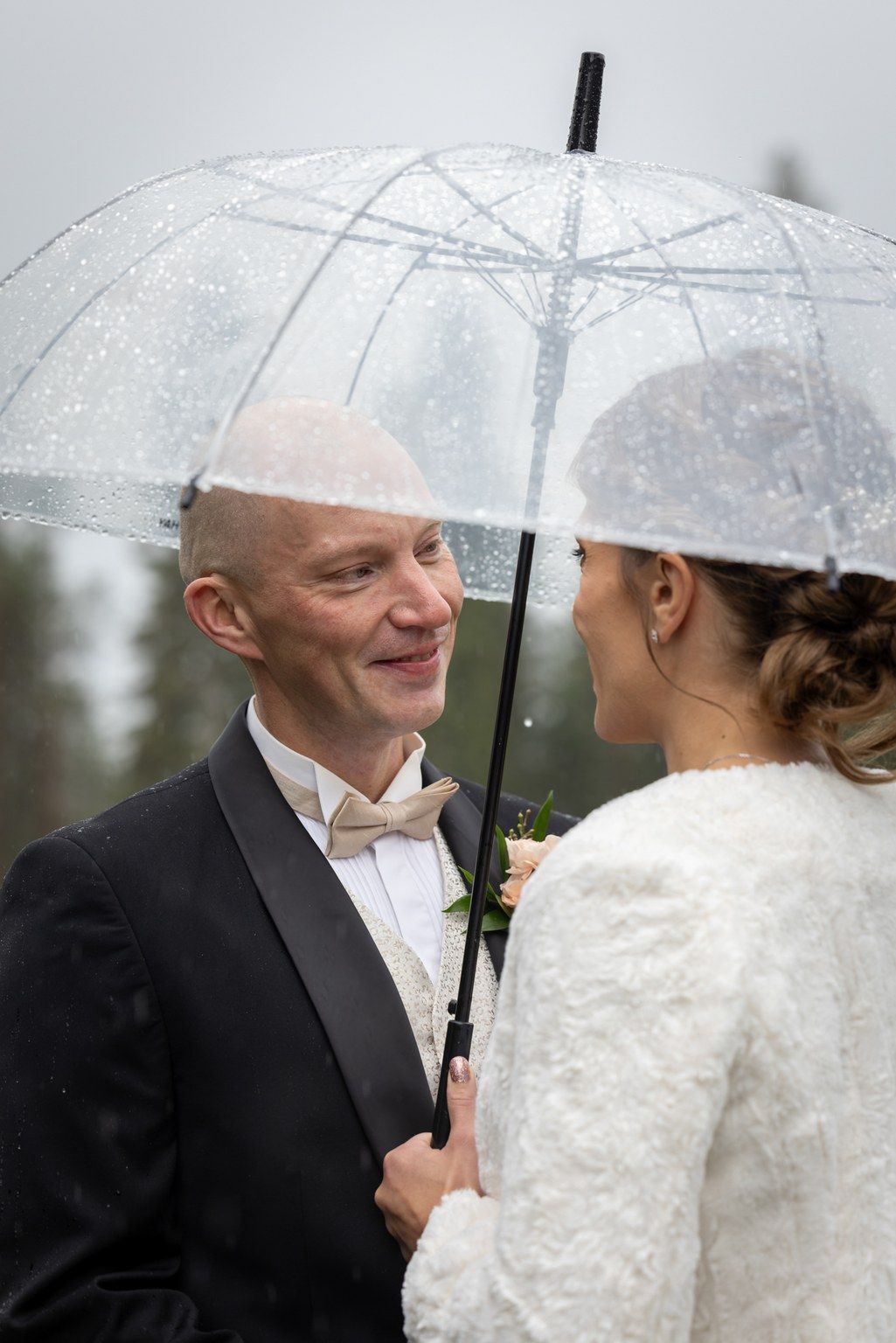 A couple shares an intimate moment under a clear umbrella in the rain on their wedding day.
