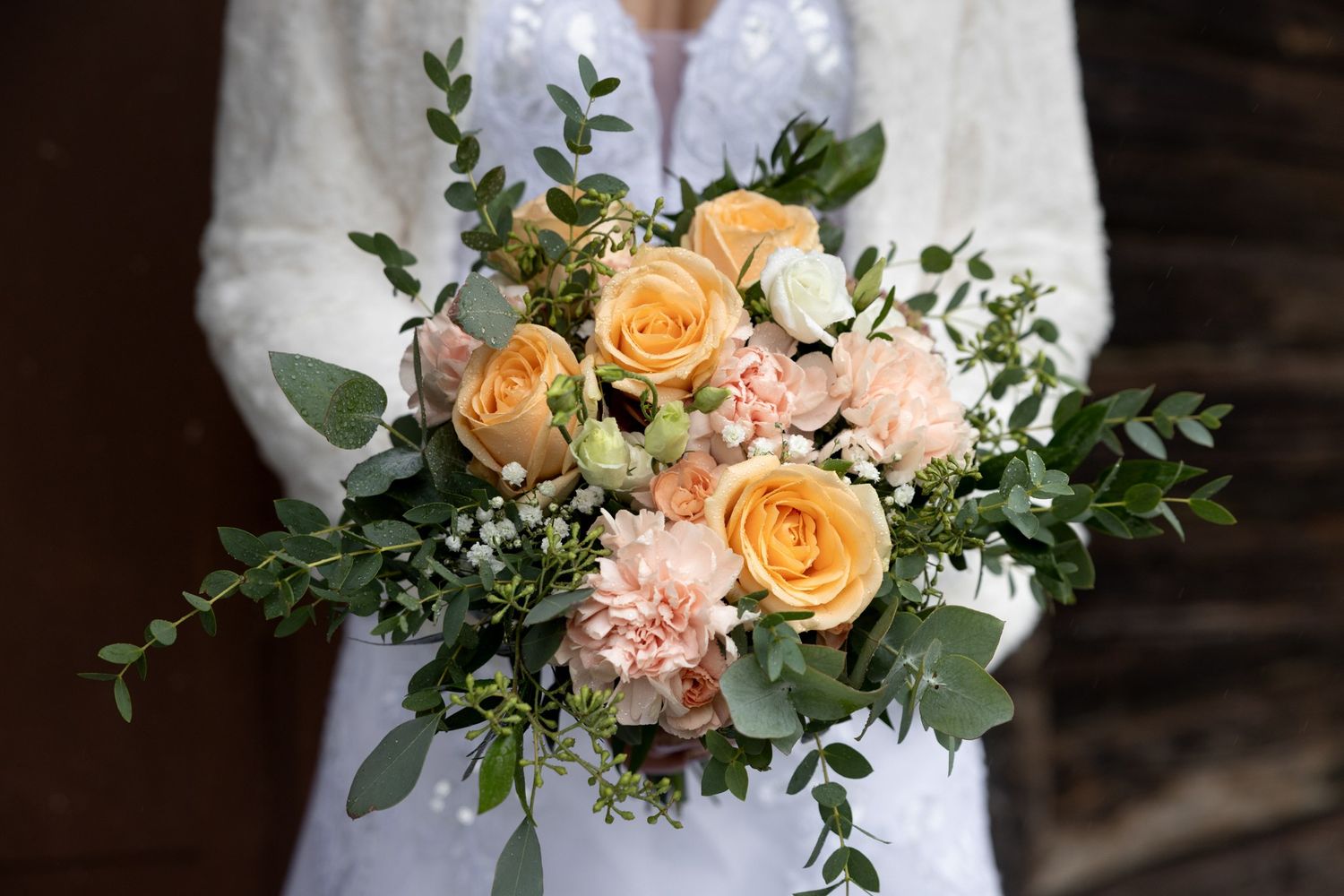 A romantic wedding couple embracing in a garden setting with peach and white floral arrangements.