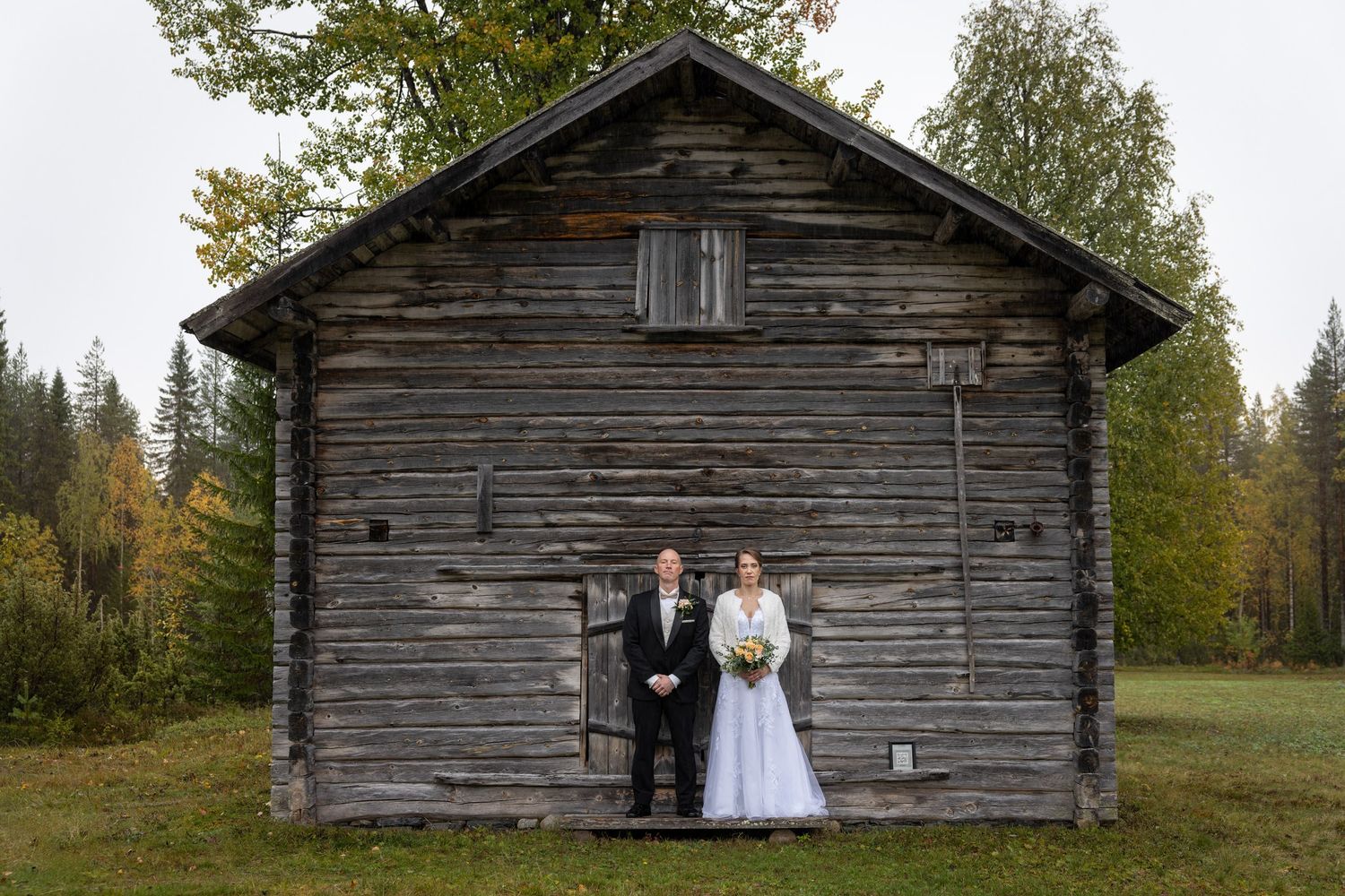 A rustic wooden barn provides a charming backdrop for a wedding ceremony in a scenic forest setting.