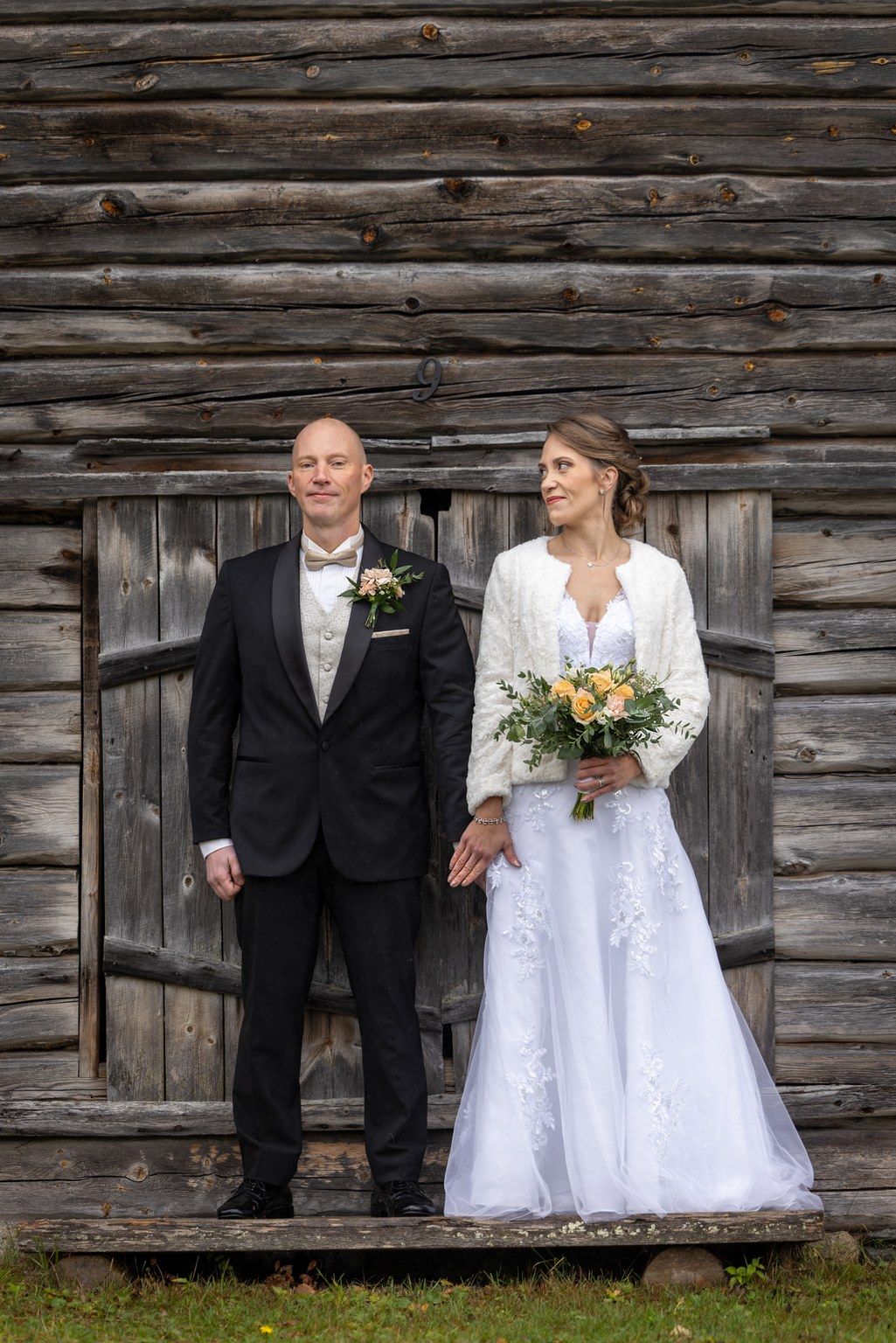 A rustic wedding couple poses against a weathered log cabin wall in a series of romantic portraits.
