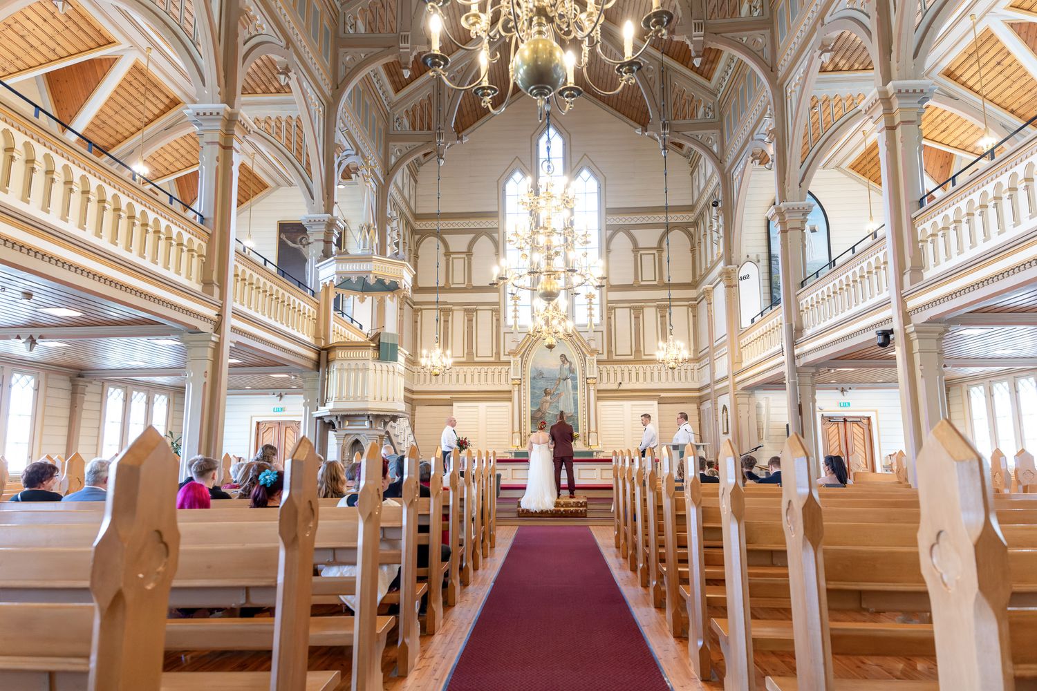 Interior panorama of a grand church with ornate white walls, wooden pews, and red carpet leading to the altar.