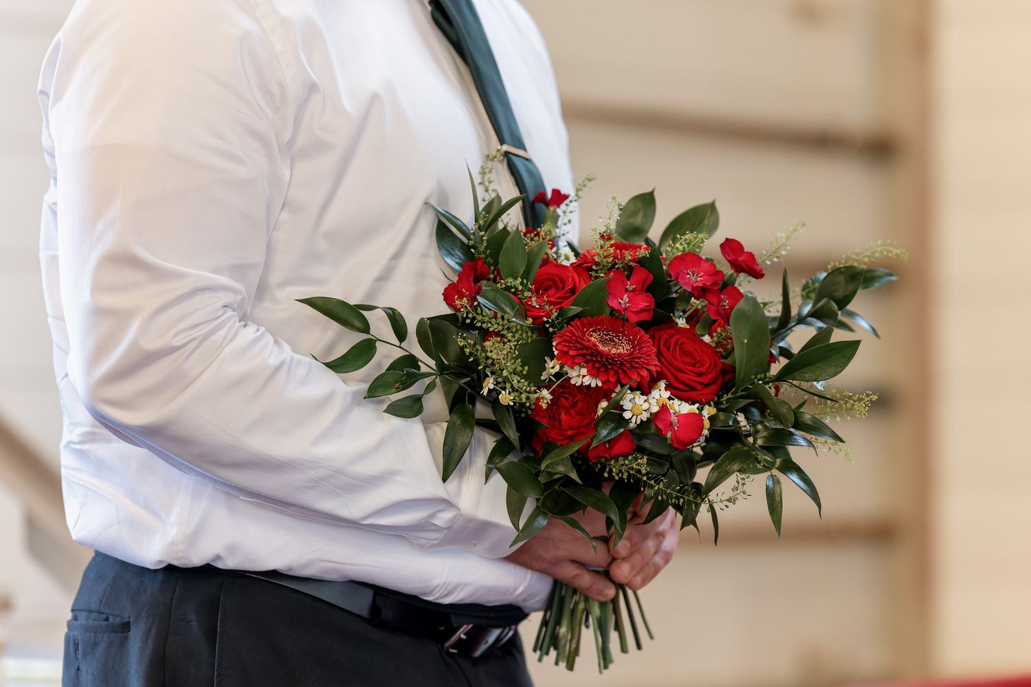 A wedding couple holding red and white floral bouquets stand together during their winter ceremony.