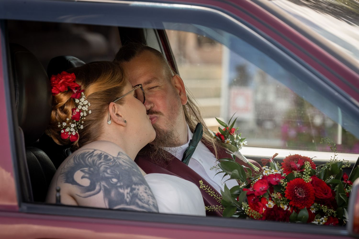 A couple shares a tender moment in a car decorated with red roses on their wedding day.