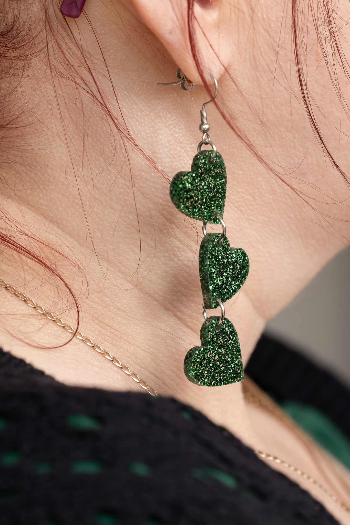 Close-up sequence showing sparkly green heart-shaped dangle earrings against a light skin tone background.
