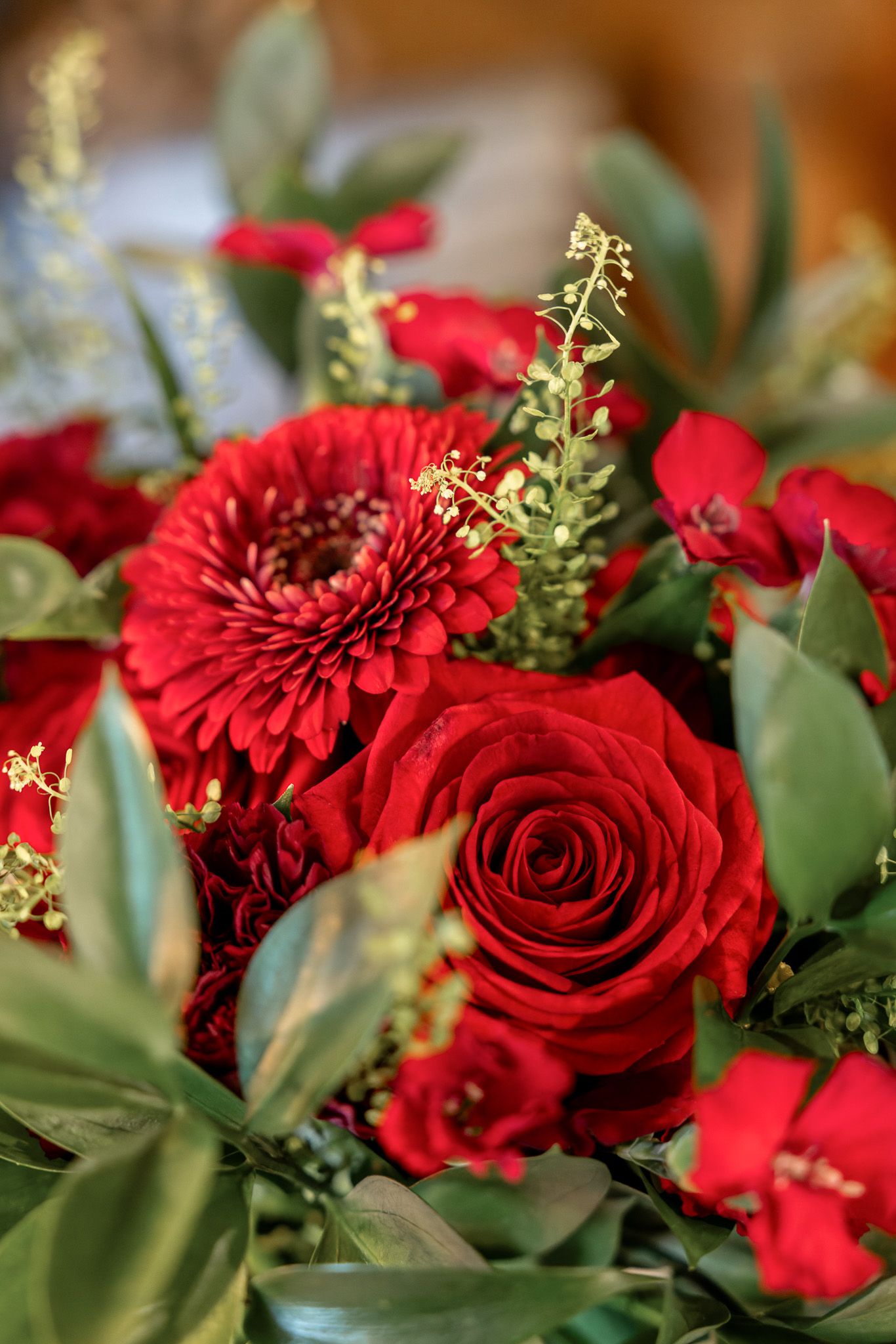 Close-up of vibrant red roses and carnations with delicate green foliage in a romantic floral arrangement.