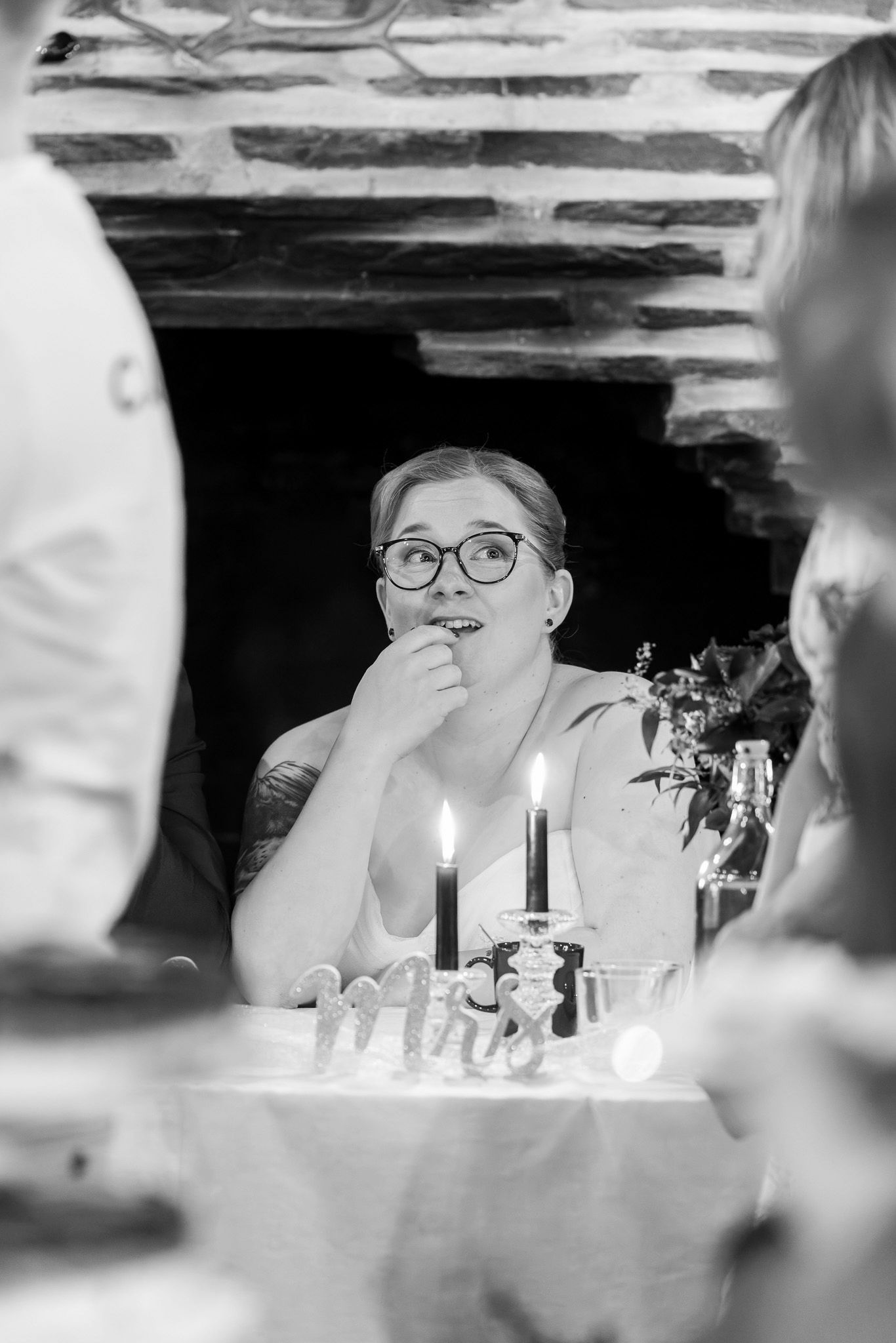 Black and white candid photograph of a dinner party scene with candlelight and glasses on the table.