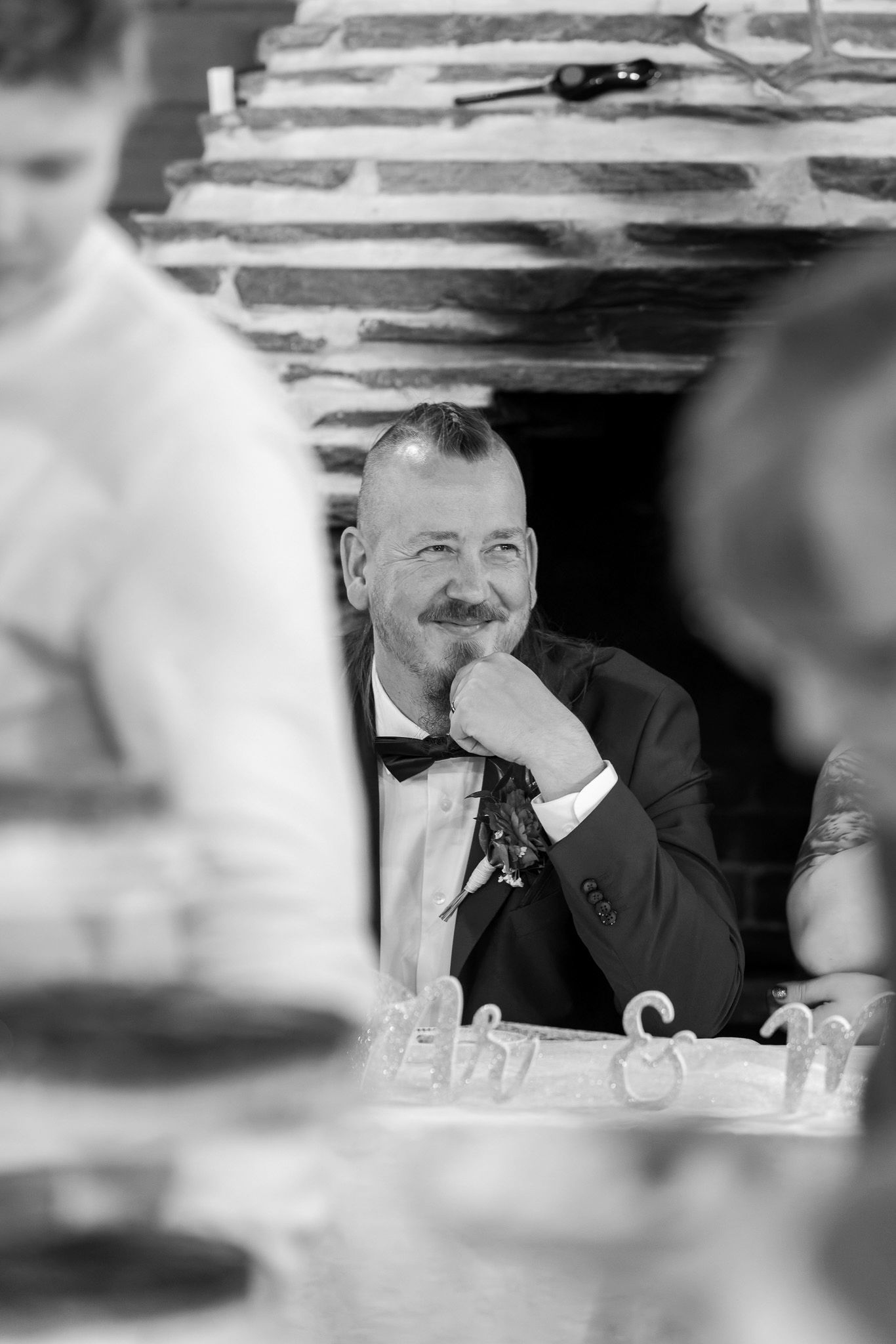 A black and white candid photo shows someone smiling and looking to the side during what appears to be a formal event.