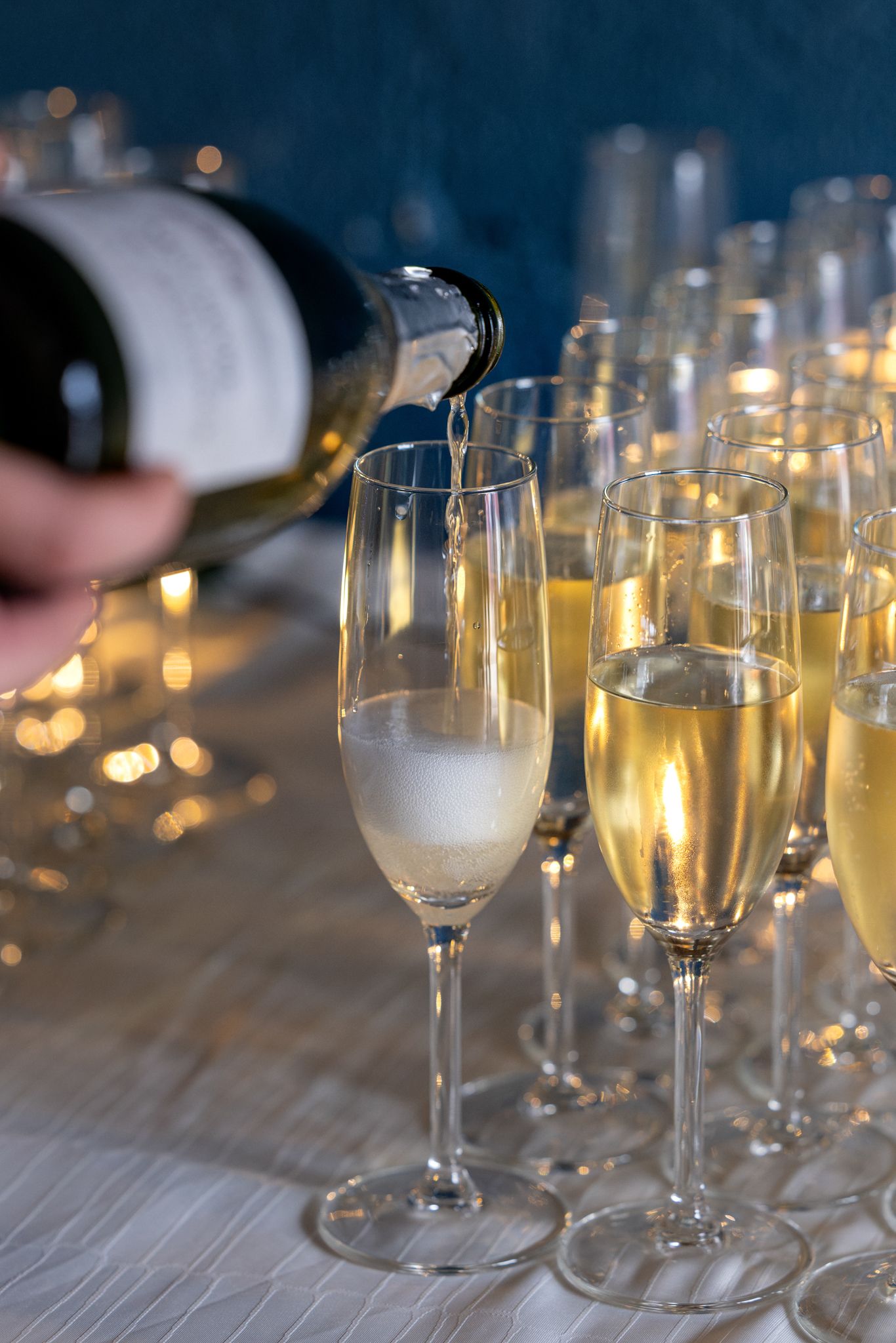 Champagne being poured into elegant flute glasses at a celebration event with golden bokeh lights in background.