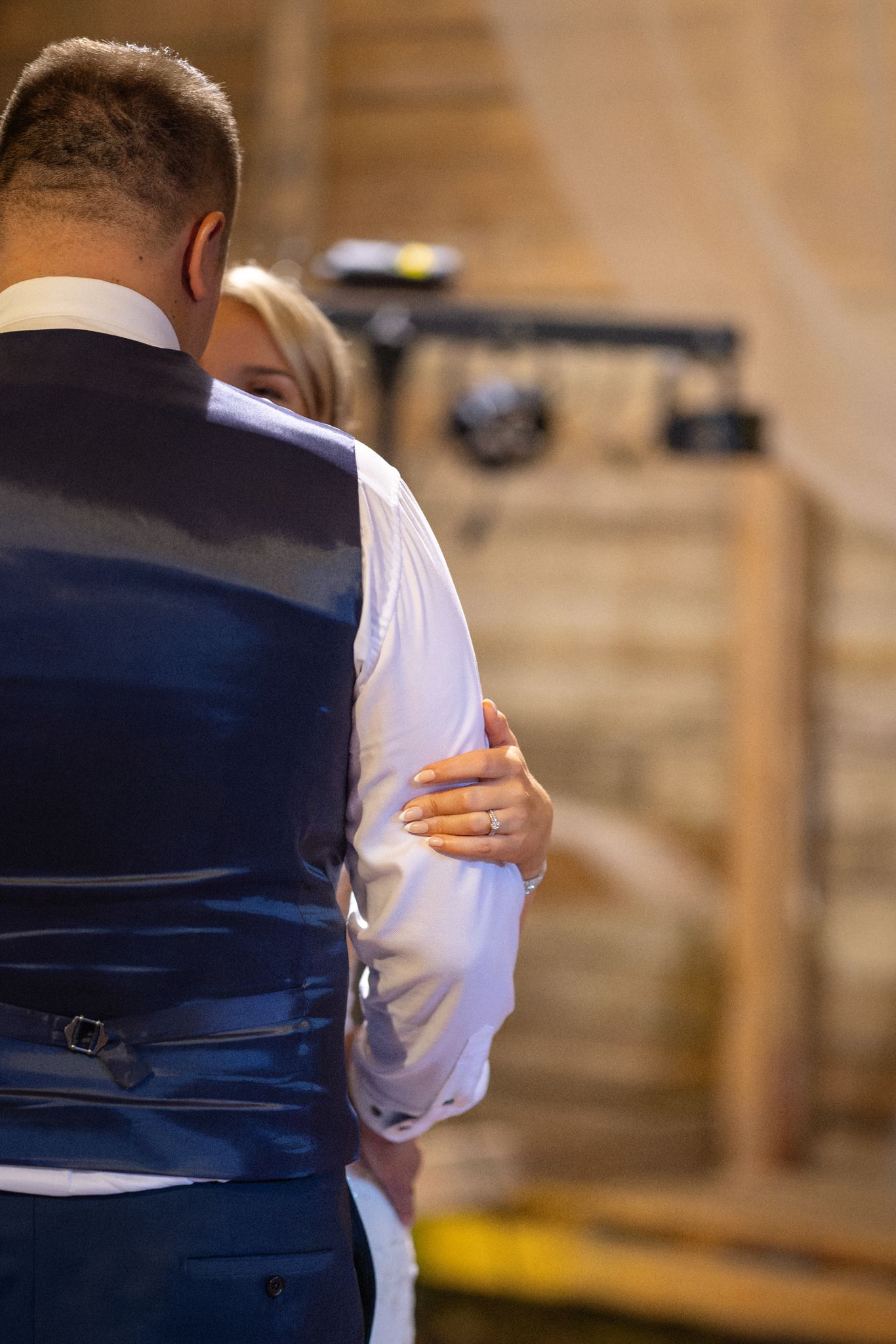 Couple sharing first dance at wedding, bride's hand with ring visible on groom's back in blue vest.