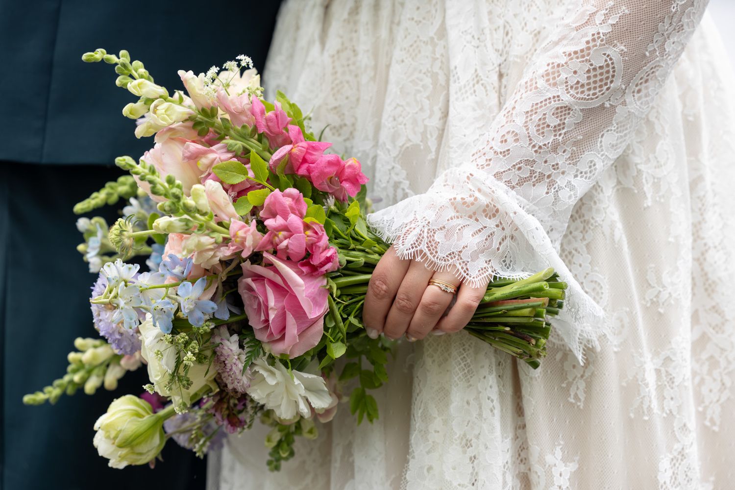 Bride in lace wedding dress holding a colorful bouquet of pink roses, blue and green flowers at a wedding ceremony.