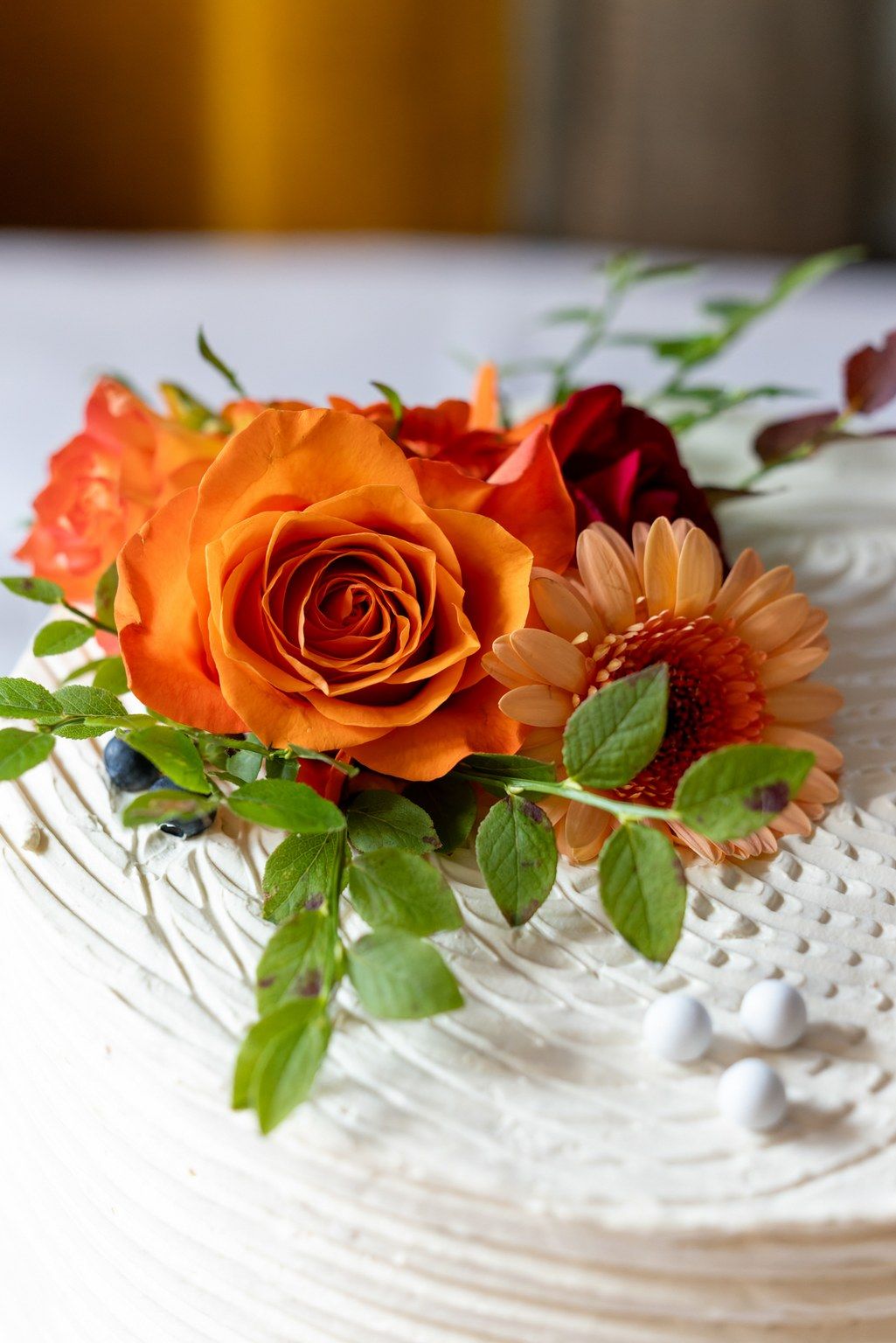 Orange roses and gerbera daisies arranged on a white lace doily with green foliage create an elegant floral display.
