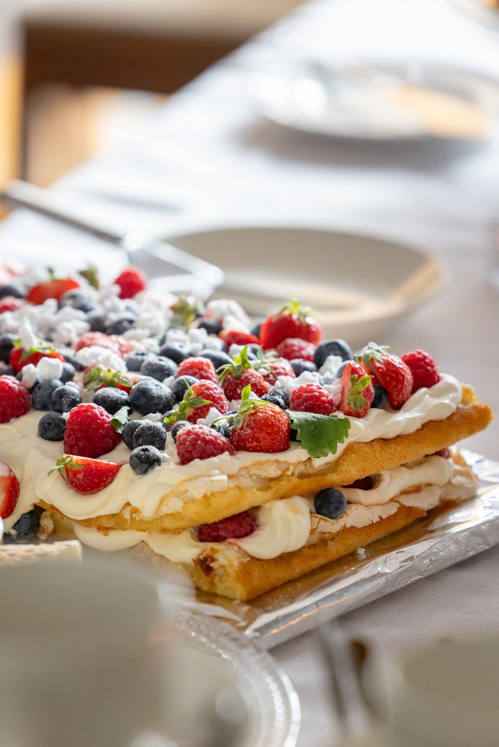 Fresh berry millefeuille dessert with layers of puff pastry, whipped cream, blueberries, raspberries and mint leaves.
